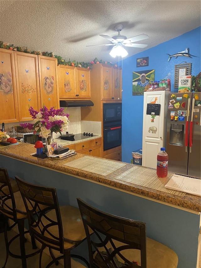 kitchen with a kitchen bar, a textured ceiling, black appliances, and kitchen peninsula