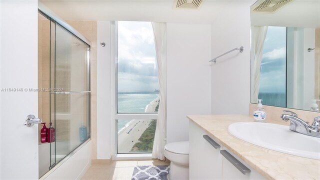 full bathroom featuring vanity, tile patterned flooring, toilet, enclosed tub / shower combo, and a water view