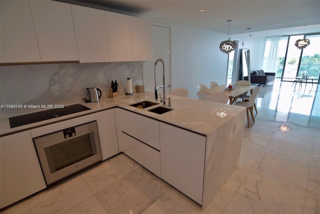 kitchen with white cabinetry, a chandelier, light stone counters, kitchen peninsula, and sink