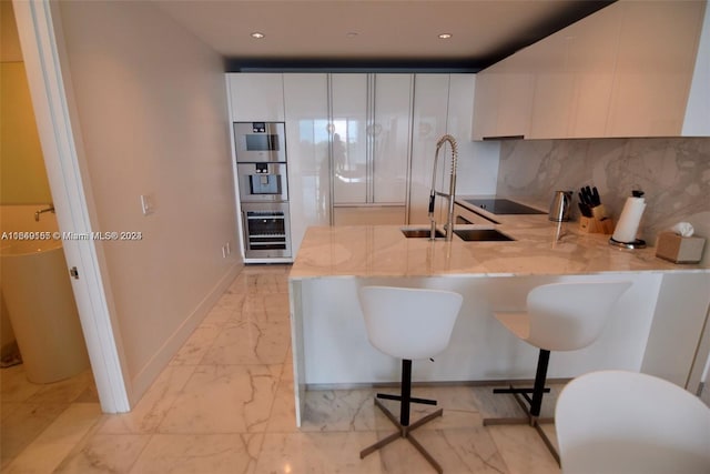 kitchen with white cabinetry, sink, kitchen peninsula, a kitchen breakfast bar, and decorative backsplash