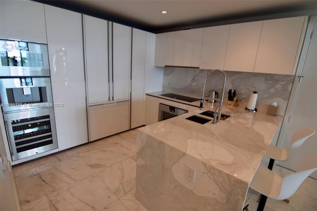 kitchen featuring tasteful backsplash, light stone countertops, wine cooler, and white cabinets