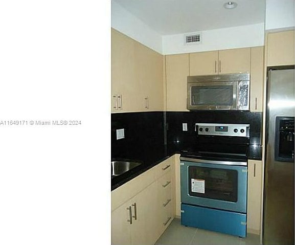 kitchen featuring backsplash, light tile patterned floors, cream cabinets, appliances with stainless steel finishes, and sink