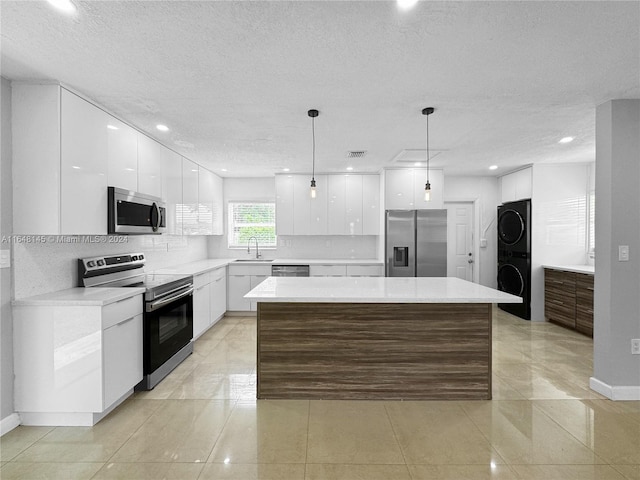 kitchen featuring appliances with stainless steel finishes, a center island, white cabinetry, and stacked washer / drying machine