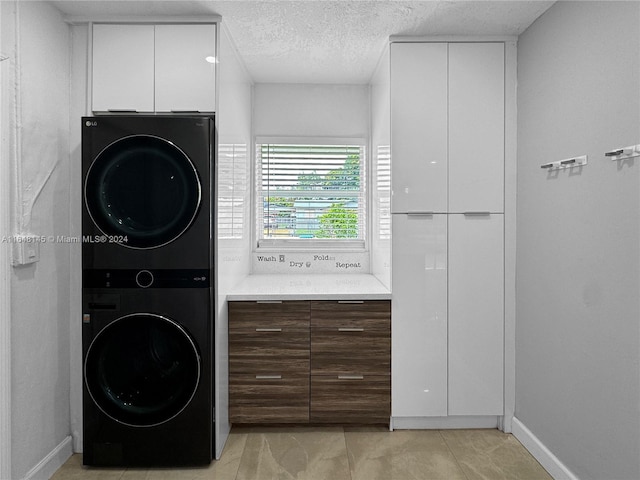 washroom featuring a textured ceiling, light tile patterned flooring, cabinets, and stacked washer and dryer