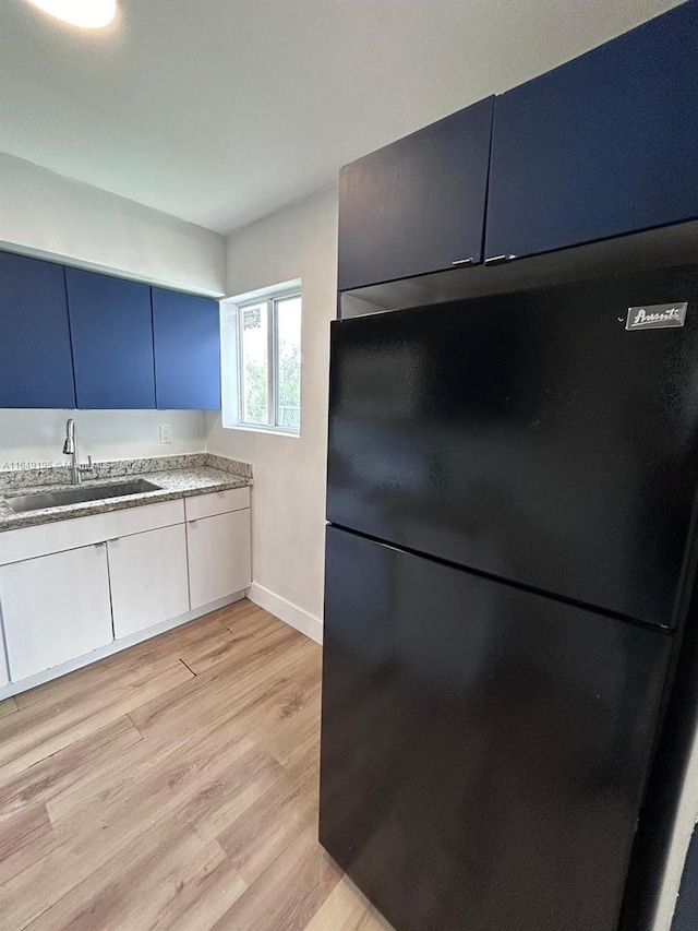 kitchen with light wood-type flooring, sink, blue cabinetry, and black fridge