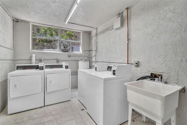 laundry room with washing machine and clothes dryer, a textured ceiling, and sink