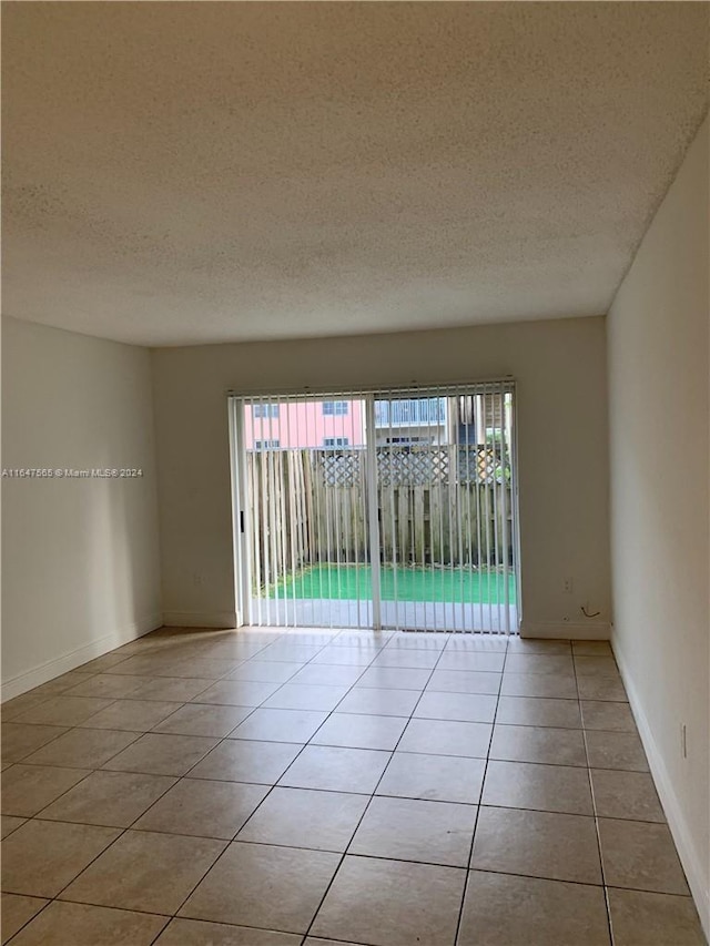 spare room featuring light tile patterned flooring, a textured ceiling, and baseboards