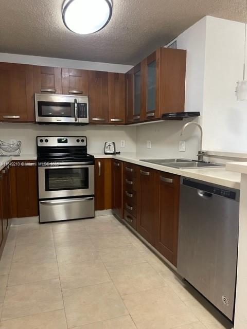 kitchen featuring a textured ceiling, sink, light tile patterned floors, and appliances with stainless steel finishes