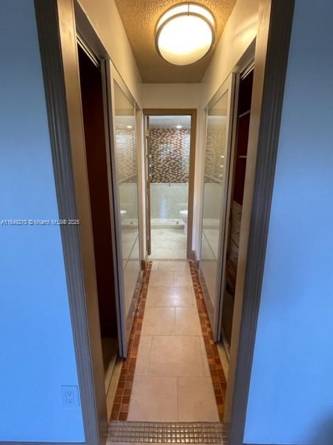 hallway with a textured ceiling and light tile patterned flooring