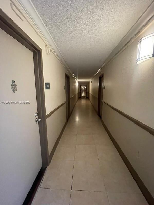 corridor with crown molding, tile patterned floors, and a textured ceiling