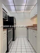 kitchen featuring a paneled ceiling, appliances with stainless steel finishes, light tile patterned floors, and white cabinetry