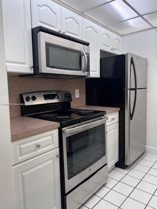 kitchen featuring stainless steel appliances, light tile patterned floors, backsplash, and white cabinetry