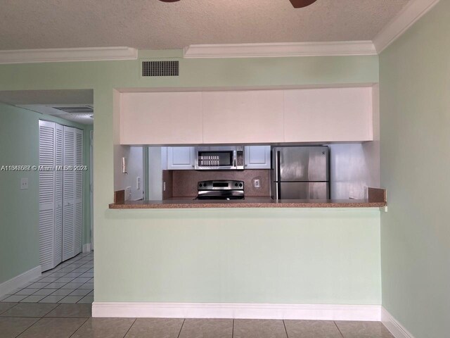 kitchen with tile patterned flooring, appliances with stainless steel finishes, a textured ceiling, and ornamental molding