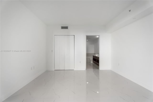 unfurnished bedroom featuring ensuite bath, light tile patterned floors, and a closet