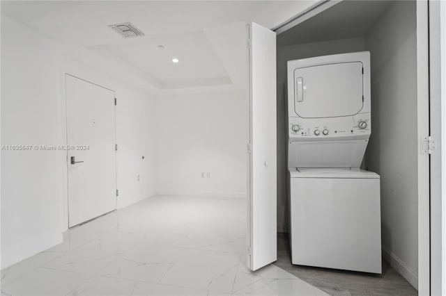 laundry room featuring stacked washing maching and dryer and light tile patterned floors