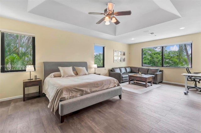 bedroom with hardwood / wood-style flooring, ceiling fan, a raised ceiling, and multiple windows