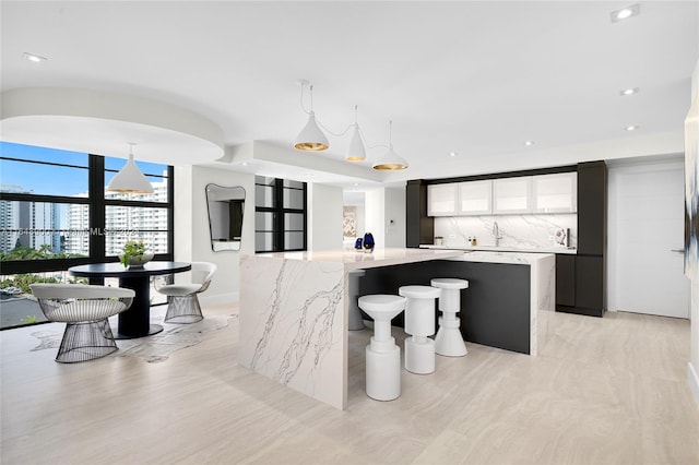 kitchen featuring a spacious island, backsplash, decorative light fixtures, light stone countertops, and a breakfast bar