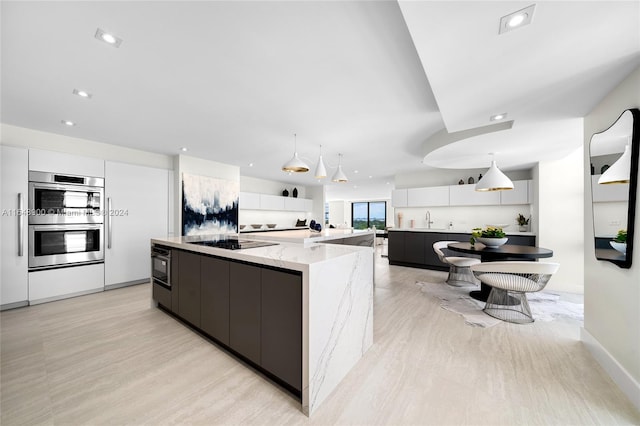 kitchen featuring hanging light fixtures, a large island, light stone counters, and white cabinetry