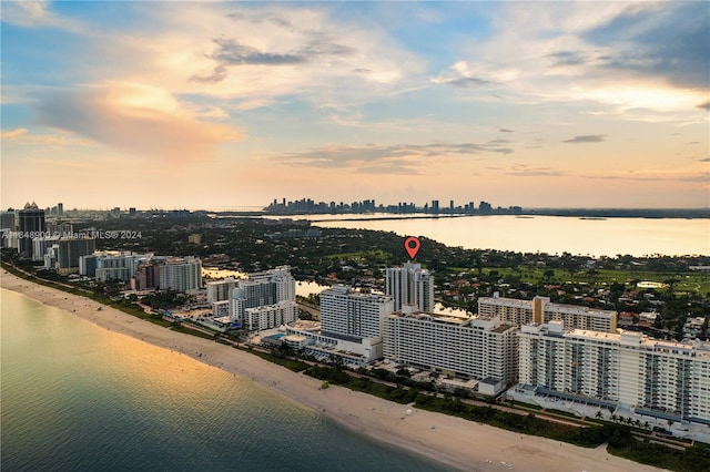 aerial view at dusk with a water view and a view of the beach