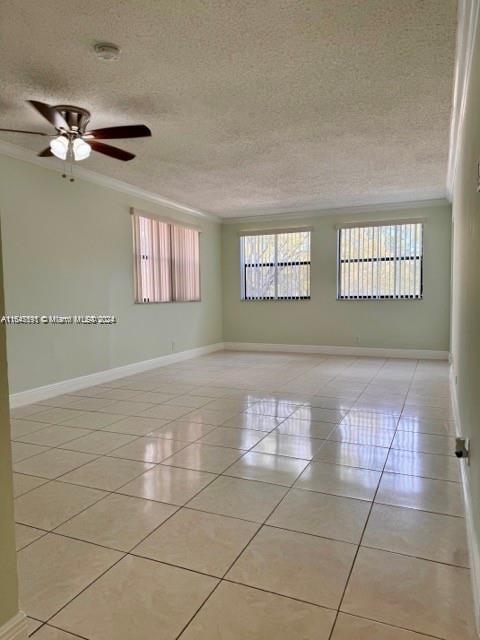 empty room with ceiling fan, a textured ceiling, light tile patterned flooring, and ornamental molding