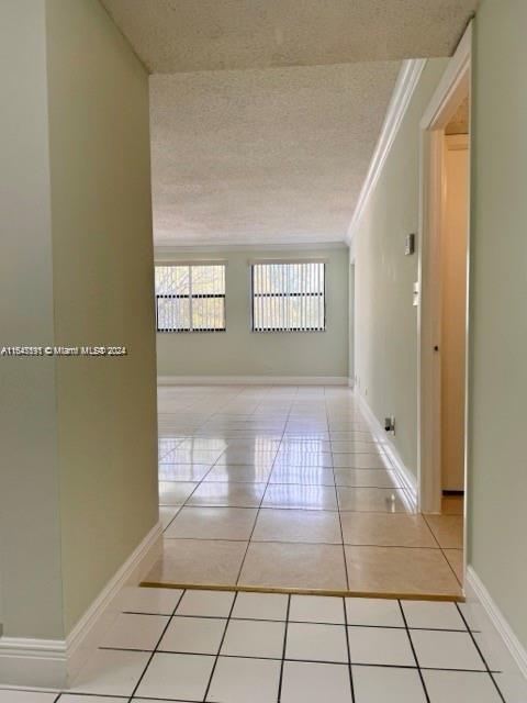 hallway with a textured ceiling, ornamental molding, and light tile patterned floors