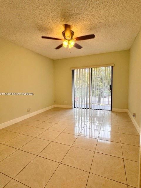 empty room with ceiling fan, light tile patterned floors, and a textured ceiling