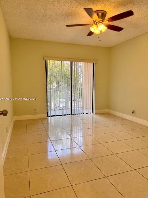 empty room featuring ceiling fan, light tile patterned floors, and a textured ceiling