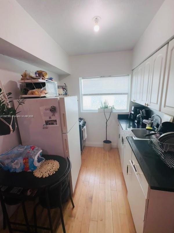 kitchen featuring light wood finished floors, white appliances, dark countertops, white cabinetry, and a sink