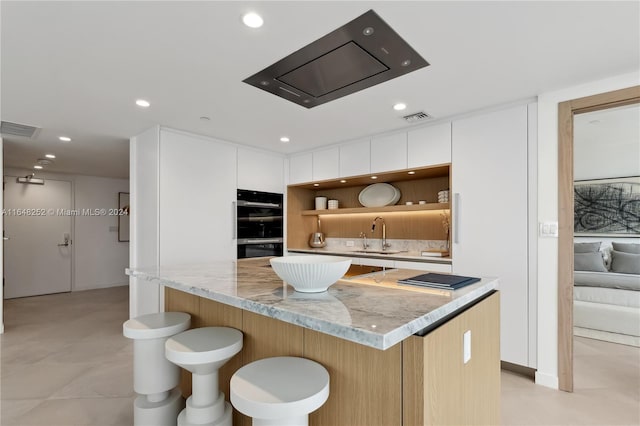 kitchen featuring white cabinets, a center island, light stone counters, and sink