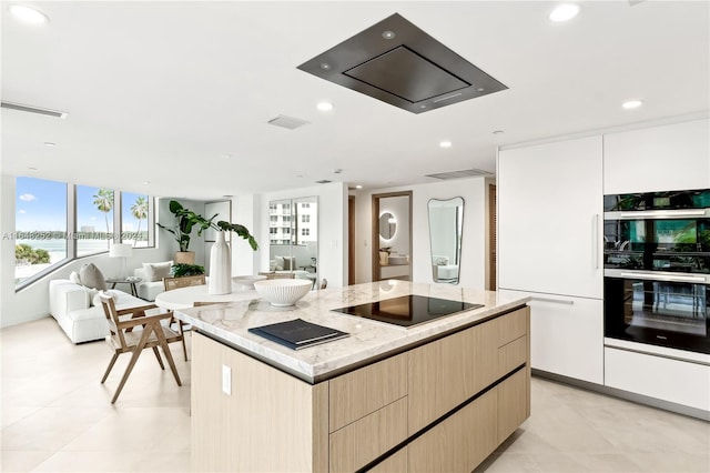 kitchen with light brown cabinets, a kitchen island, light stone counters, white cabinets, and black appliances