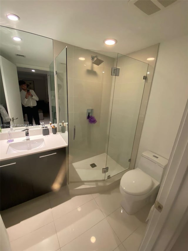 bathroom featuring a shower with shower door, toilet, vanity, and tile patterned floors