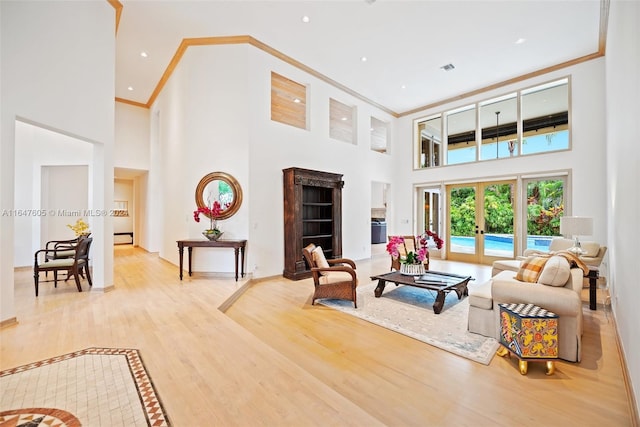 living room with crown molding, a towering ceiling, light wood-type flooring, and french doors