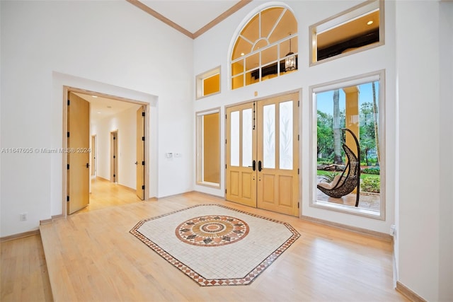 foyer featuring a towering ceiling, french doors, ornamental molding, and light hardwood / wood-style floors