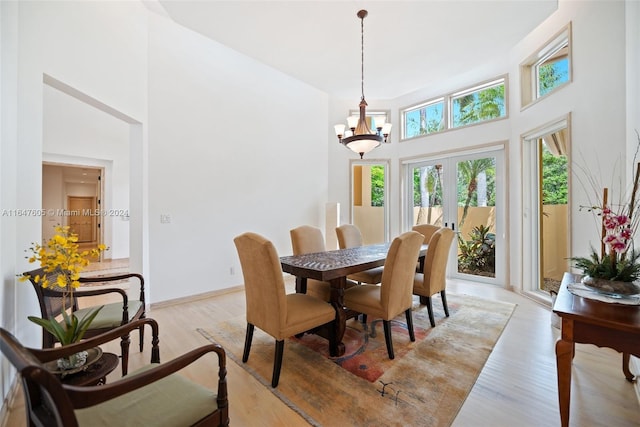 dining room featuring light wood-type flooring, french doors, an inviting chandelier, and a towering ceiling