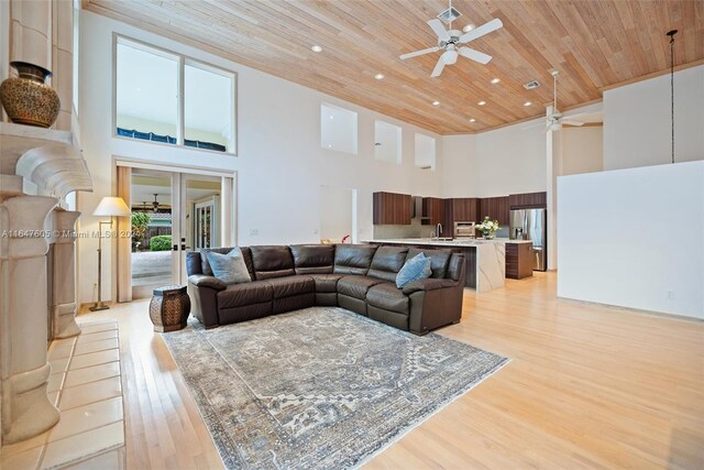 living room featuring a high ceiling, light hardwood / wood-style flooring, sink, ceiling fan, and wood ceiling