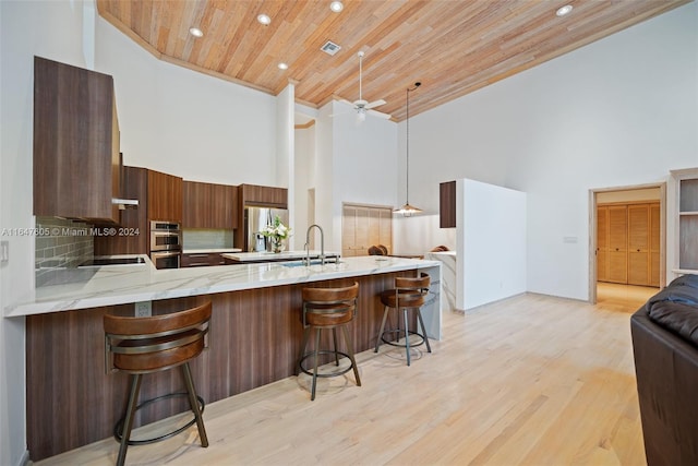 kitchen featuring high vaulted ceiling, wood ceiling, a kitchen bar, and kitchen peninsula