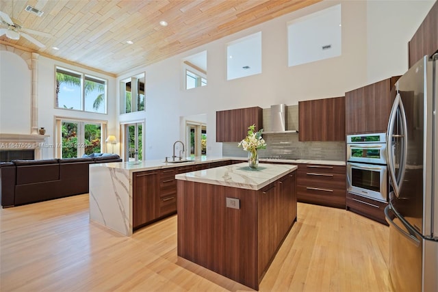 kitchen featuring kitchen peninsula, stainless steel appliances, wall chimney exhaust hood, and light hardwood / wood-style floors