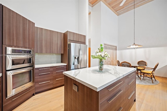 kitchen with pendant lighting, a high ceiling, light hardwood / wood-style flooring, stainless steel appliances, and decorative backsplash