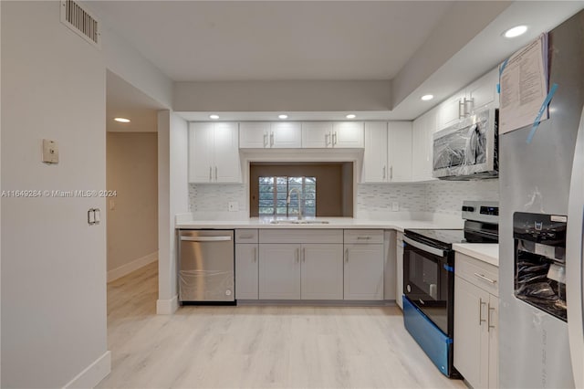 kitchen with light hardwood / wood-style floors, stainless steel appliances, sink, decorative backsplash, and white cabinetry