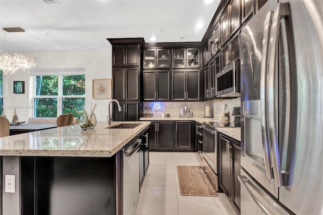 kitchen featuring light tile patterned floors, sink, hanging light fixtures, appliances with stainless steel finishes, and a center island with sink