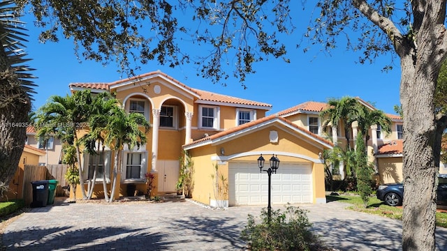 mediterranean / spanish house with an attached garage, stucco siding, a tile roof, and decorative driveway
