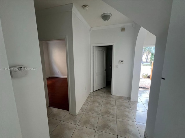 corridor with arched walkways, light tile patterned floors, and crown molding