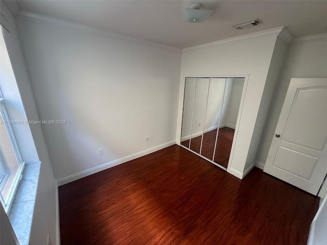 unfurnished bedroom with crown molding, a closet, and dark hardwood / wood-style floors