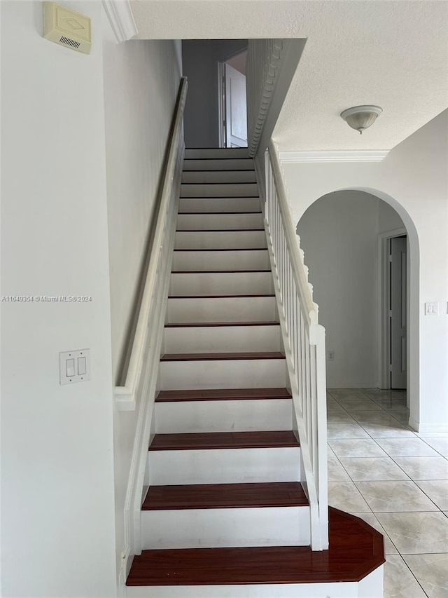 stairway featuring ornamental molding, a textured ceiling, and tile patterned flooring