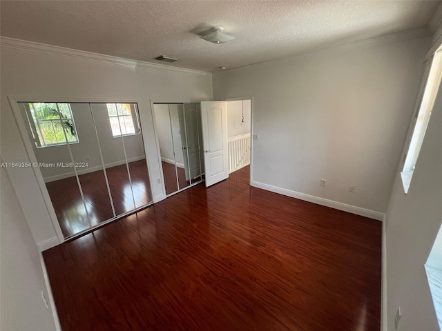 unfurnished bedroom with ornamental molding, a textured ceiling, multiple closets, and dark hardwood / wood-style floors