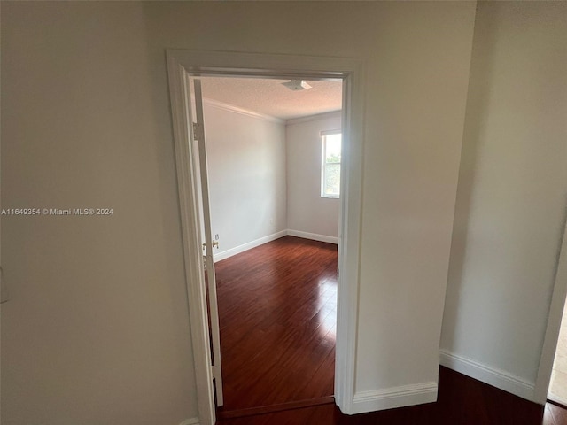 corridor featuring dark wood-type flooring, crown molding, and a textured ceiling