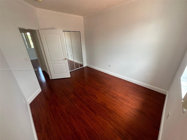 unfurnished bedroom featuring crown molding, a closet, baseboards, and dark wood finished floors