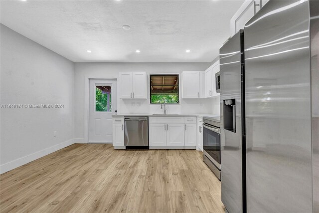 kitchen with appliances with stainless steel finishes, white cabinetry, sink, and light hardwood / wood-style floors