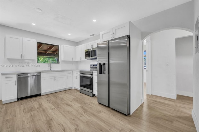 kitchen with appliances with stainless steel finishes, white cabinetry, sink, and light hardwood / wood-style floors