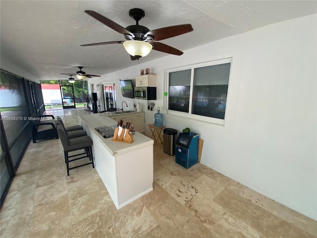 24490 SW 120th Ave, Homestead, FL 33032 - kitchen featuring stainless steel microwave, light countertops, light stone finish flooring, ceiling fan, and a kitchen bar